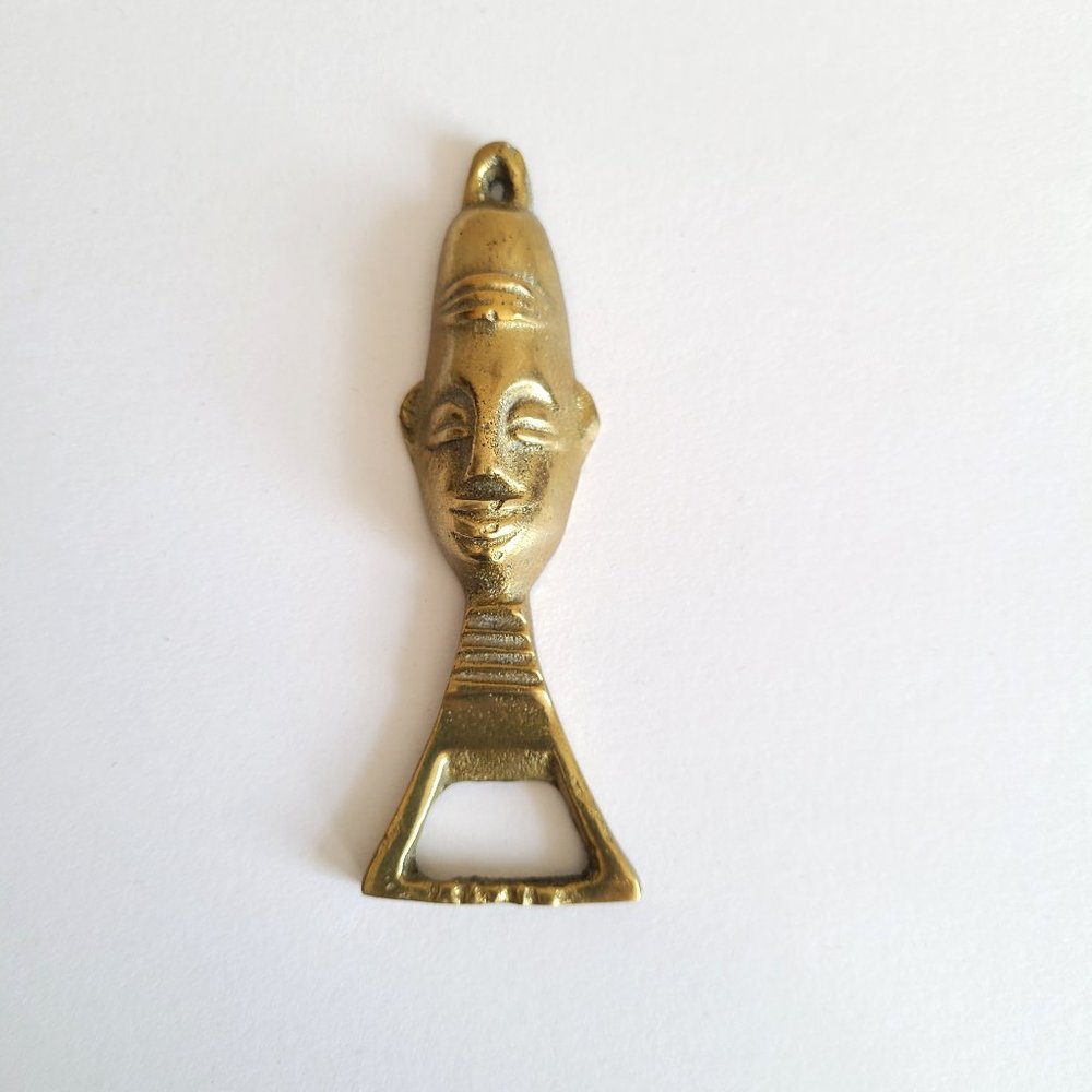 Vintage brass bottle opener with head design.